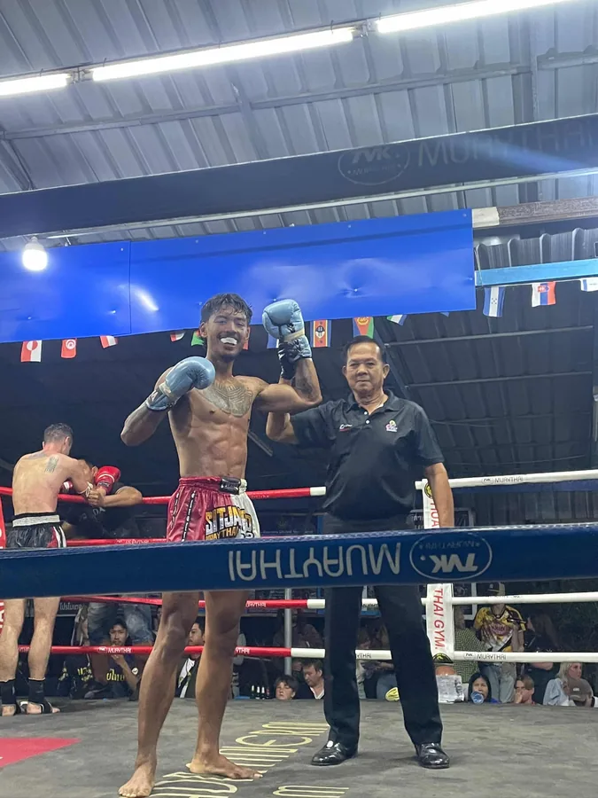 Justin in the ring after a Muay Thai fight, the referee raising his arm
